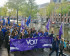 Een optocht van een grote groep Vlotters die lopen over straat. De hebben een grote banner voorop en houden vlaggen in de lucht.