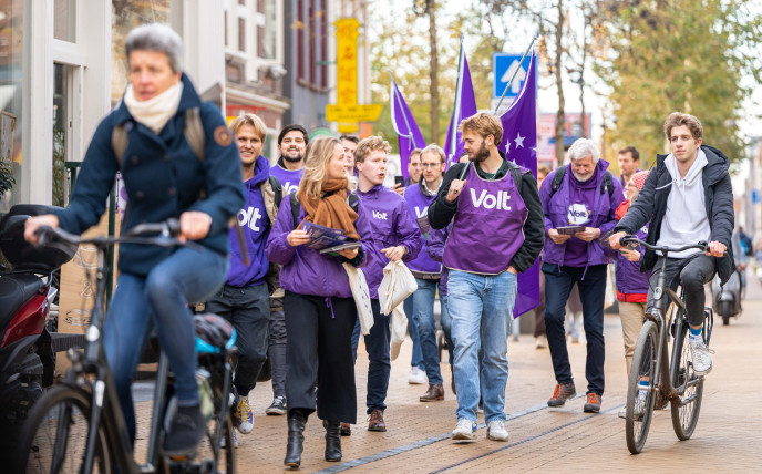 Volters lopen op straat in paarse kleding met Volt vlaggen om actie te voeren tijdens de bustour voor de 2de kamerverkiezingen 2023