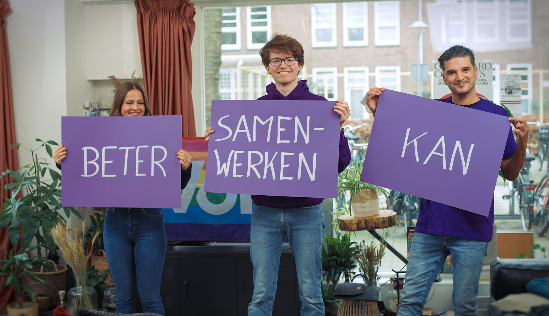 Drie personen met paarse borden waarop staat Beter Samenwerken Kan