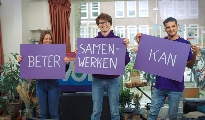 Drie personen met paarse borden waarop staat Beter Samenwerken Kan