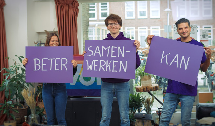 Drie personen met paarse borden waarop staat Beter Samenwerken Kan