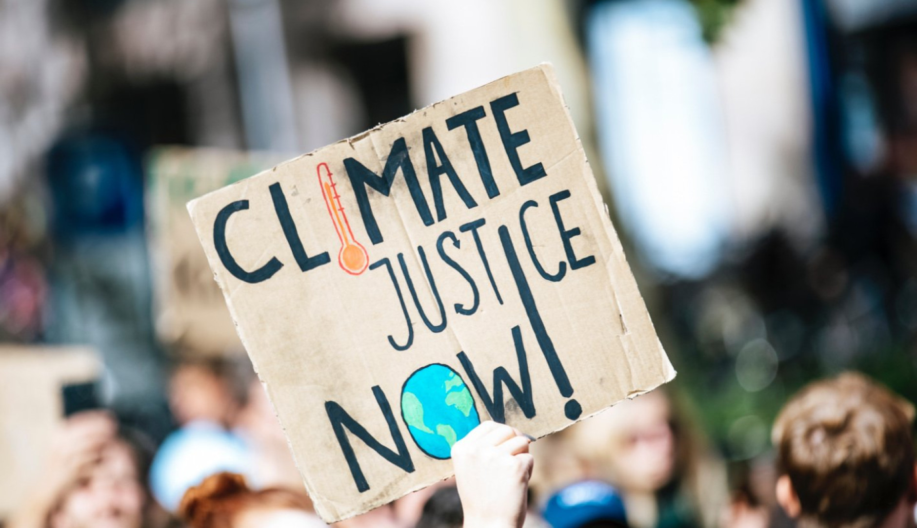 Tijdens protens houd iemand een kortonenbord omhoog met de tekst: Climate justice now