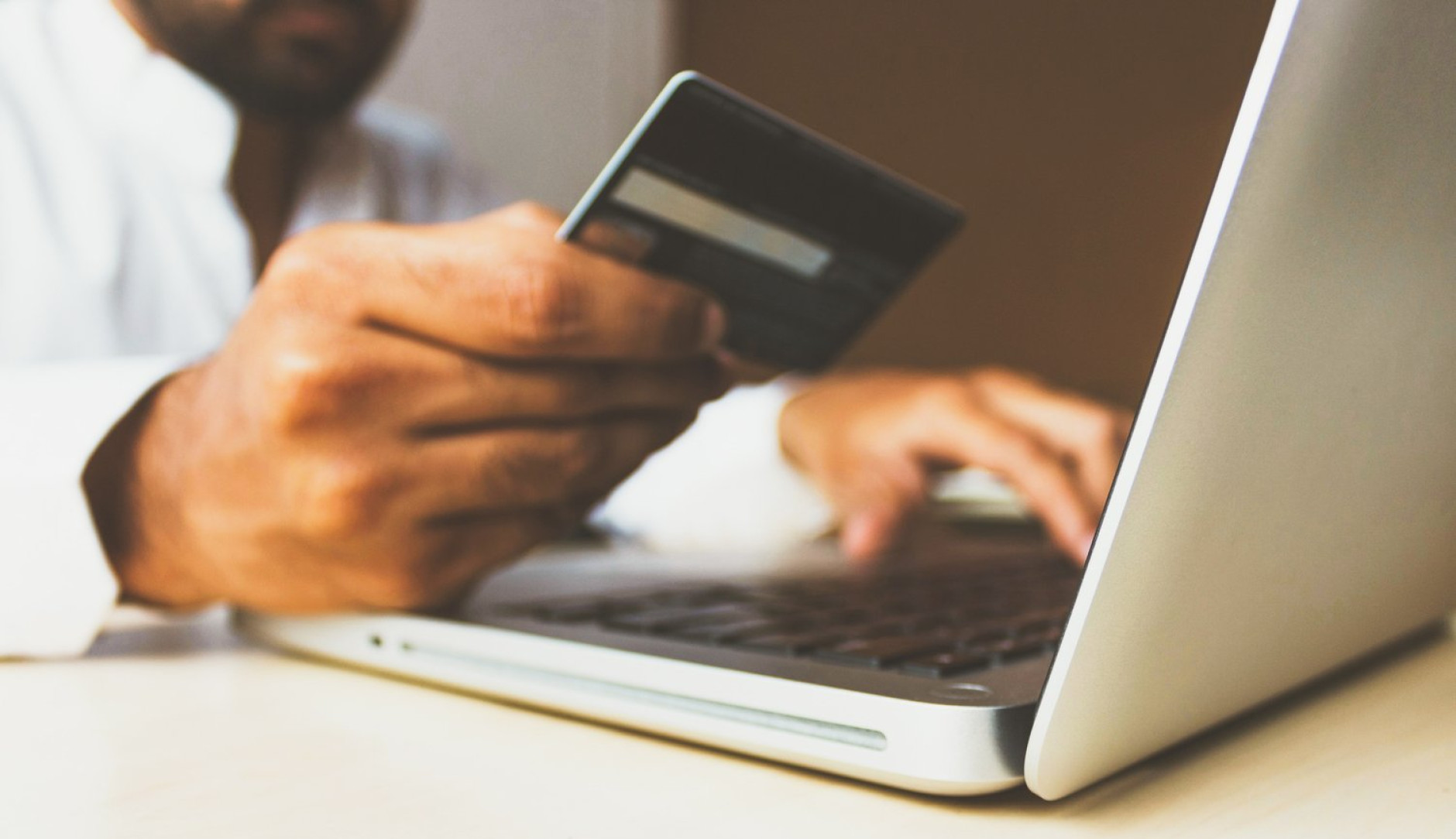 Man achter computer met bankpas in zijn hand