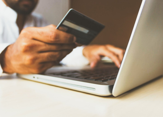 Man achter computer met bankpas in zijn hand