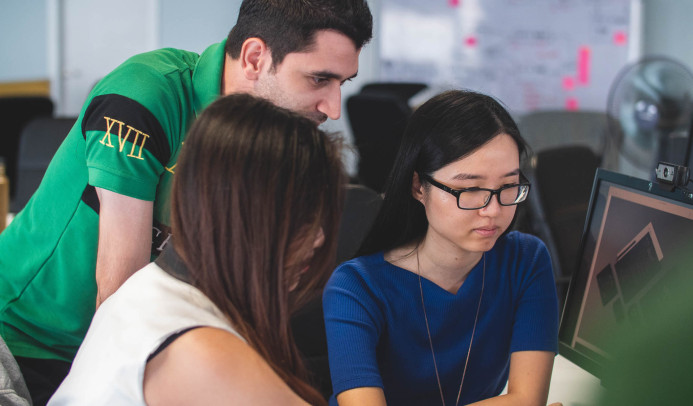 Drie mensen die naar een computer kijken en overleggen