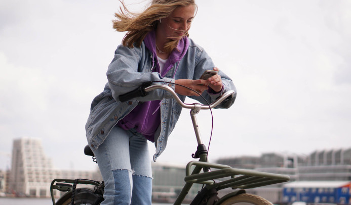 Een tienermeisje op een fiets die op haar telefoon kijkt