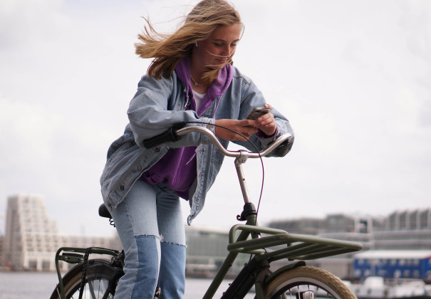 Een tienermeisje op een fiets die op haar telefoon kijkt