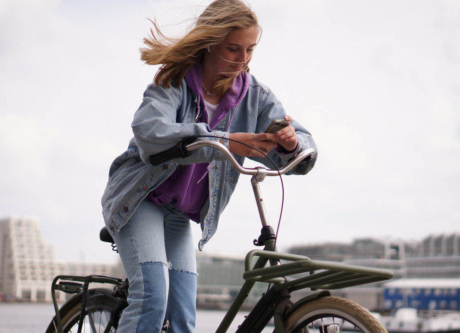 Een tienermeisje op een fiets die op haar telefoon kijkt