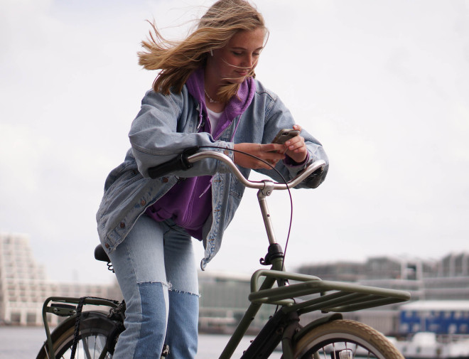 Een tienermeisje op een fiets die op haar telefoon kijkt