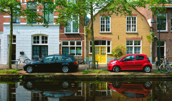 Twee auto's langs een gracht langs huizen in Nederland