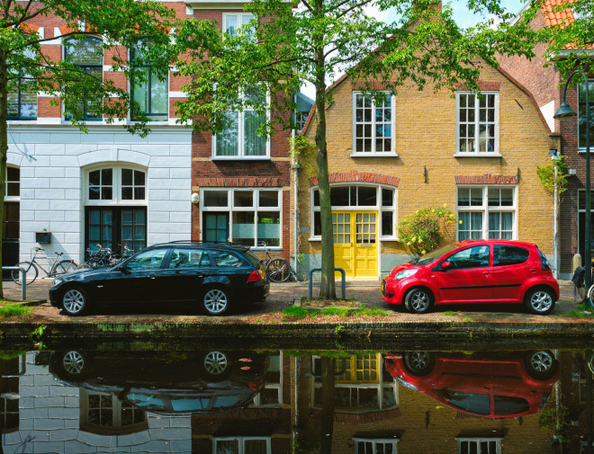 Twee auto's langs een gracht langs huizen in Nederland