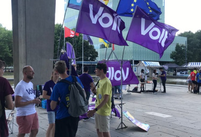 Groep mensen op een plein die aan praten zijn. Op het plein staan Volt vlaggen