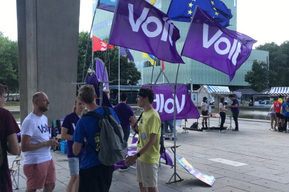 Groep mensen op een plein die aan praten zijn. Op het plein staan Volt vlaggen
