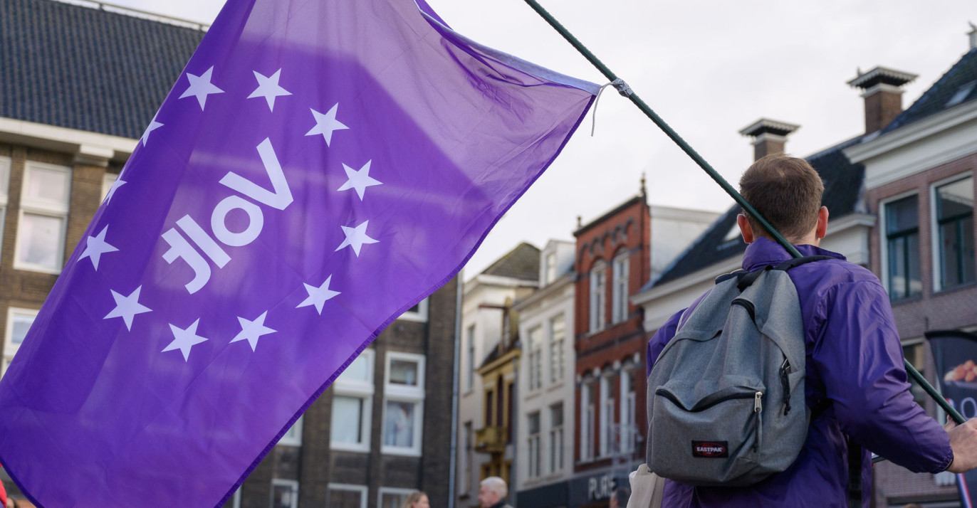 Een Volt-lid van achteren die een paarse Volt vlag vasthoudt