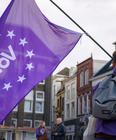 Een Volt-lid van achteren die een paarse Volt vlag vasthoudt
