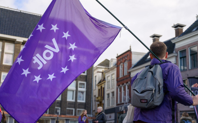 Een Volt-lid van achteren die een paarse Volt vlag vasthoudt