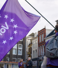 Een Volt-lid van achteren die een paarse Volt vlag vasthoudt