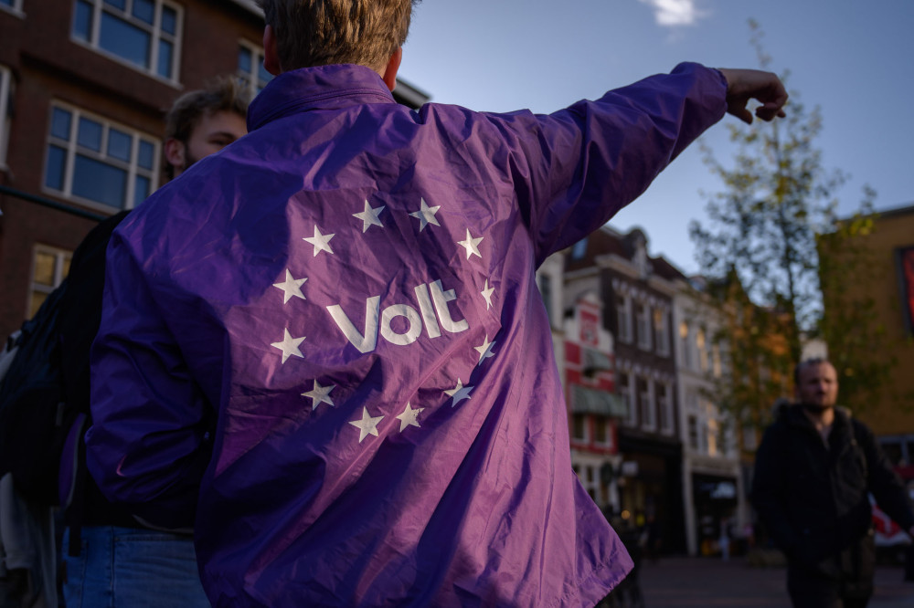 Foto van de rug van een volter die een paarse volt regen jas aanheeft. Op de rug staat het witte Volt logo met witte EU sterren er omheen