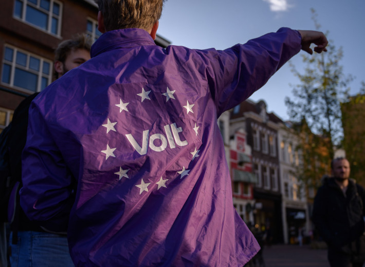 Foto van de rug van een volter die een paarse volt regen jas aanheeft. Op de rug staat het witte Volt logo met witte EU sterren er omheen